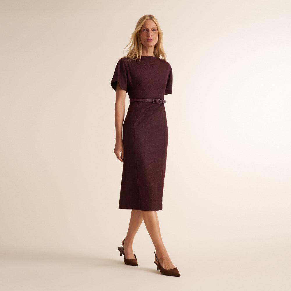 A woman modeling a short-sleeve knee-length dress in deep burgundy with a matching belt, paired with brown pointed-toe heels, against a plain beige studio background.