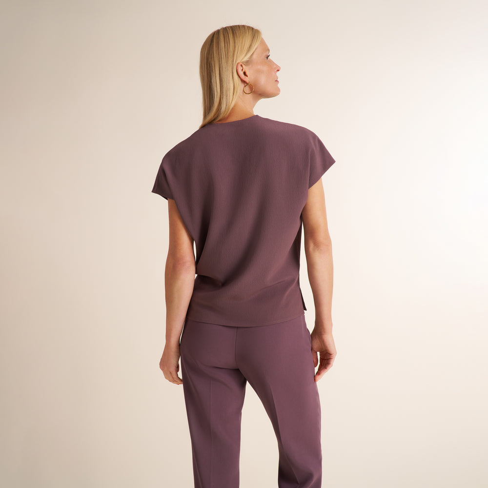 A woman shown from the back wearing a mauve short-sleeve top and matching mauve pants against a plain light beige studio background.