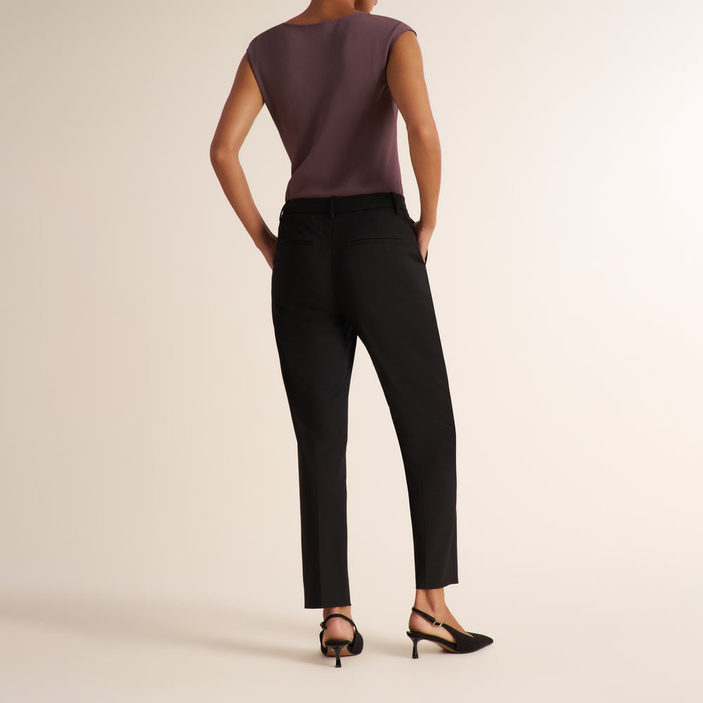Woman wearing a medium hued purple top with a tailored black blazer and matching tailored pants to make a suit