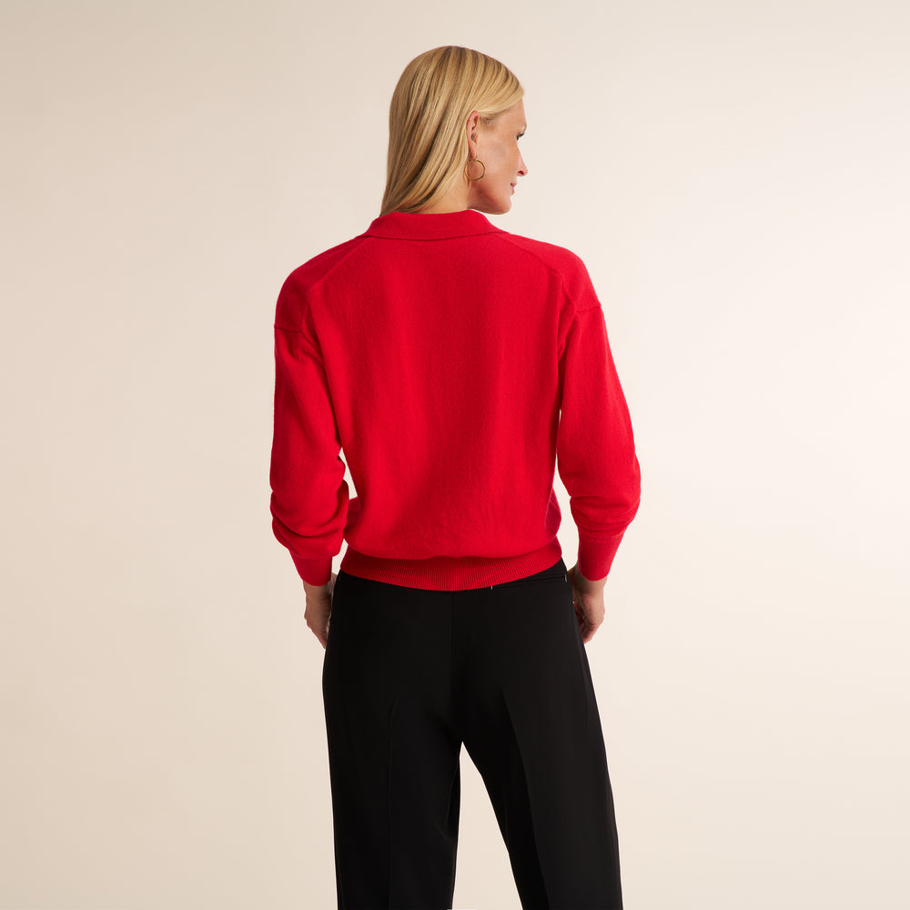 A blonde model shown from the back wearing a bright red long-sleeve crewneck sweatshirt and black pants, set against a plain beige studio background.