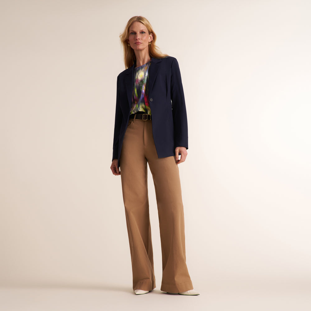 Woman wearing a navy blazer, beige wide leg pants, and printed top on a beige background