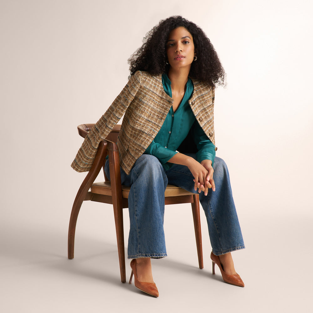 Close-up of a person wearing a textured tweed jacket in a warm brown, beige, and blue-gray mix, styled over a teal top and dark blue jeans.
