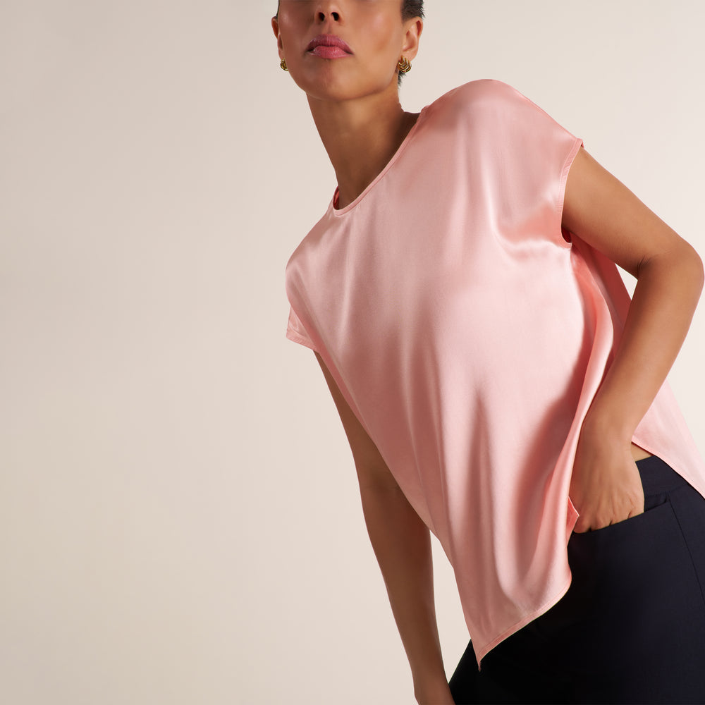 Woman wearing a flowy crew neck cap sleeve light pink silk charmeuse top with wide leg navy pants