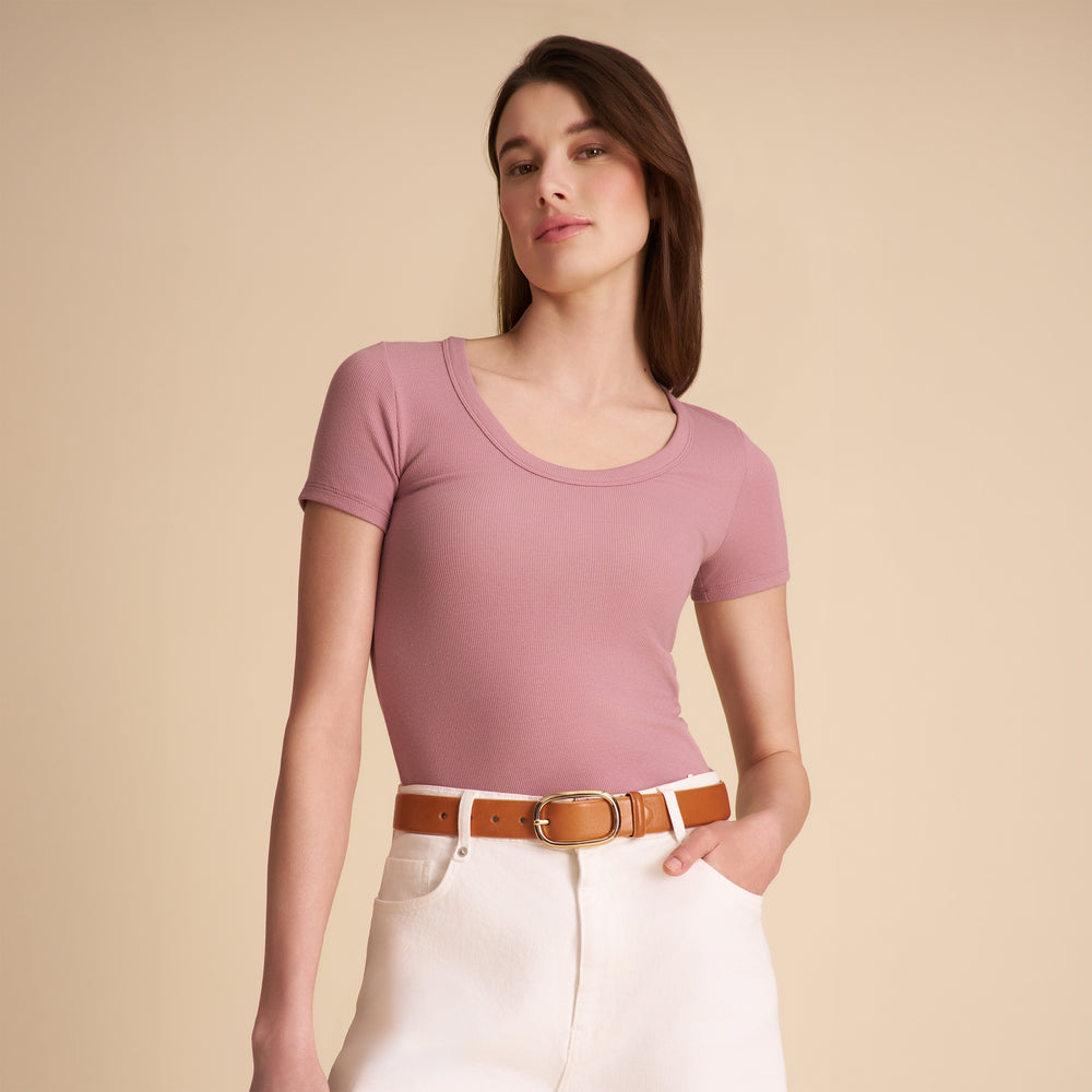 Woman wearing a pink top and white pants with a brown belt against a beige background
