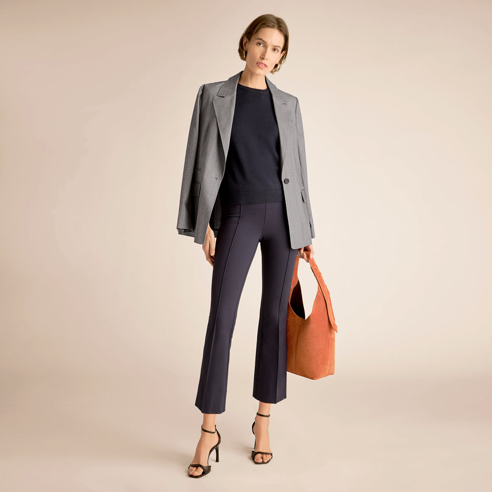 Woman in gray blazer and black pants holding an orange bag on a beige background