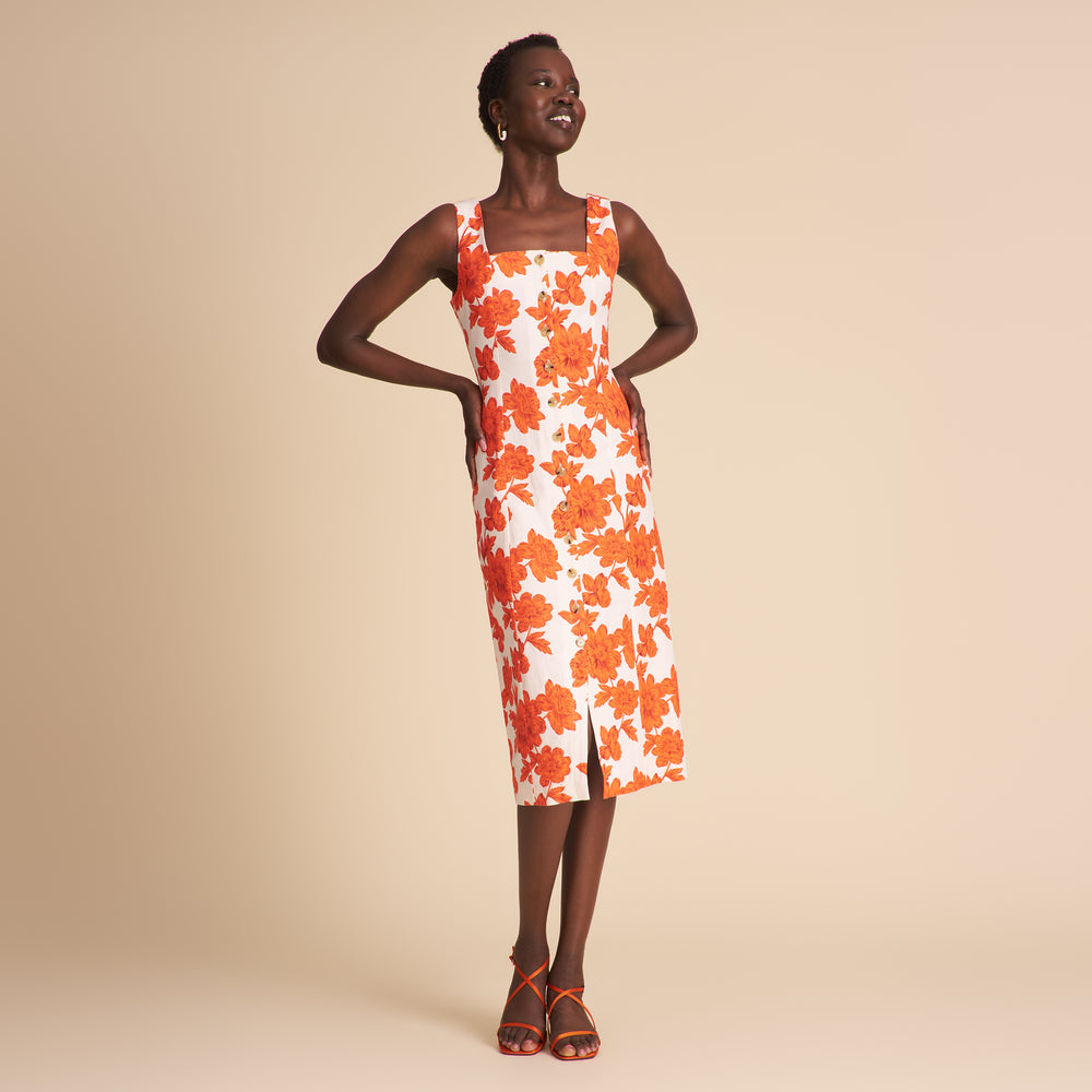 Woman in an orange and white floral dress standing on beige background