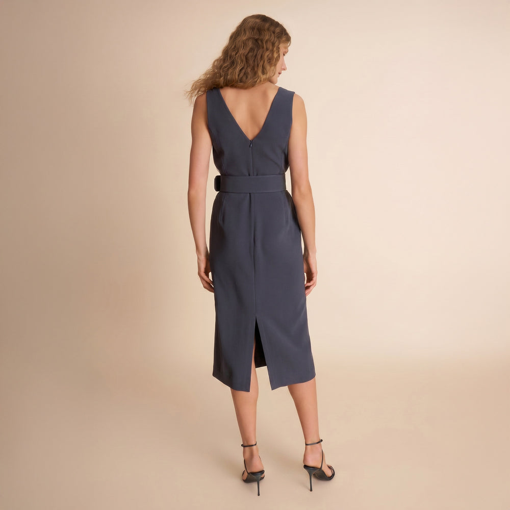 Woman wearing a sleeveless navy dress with a belt on a beige background