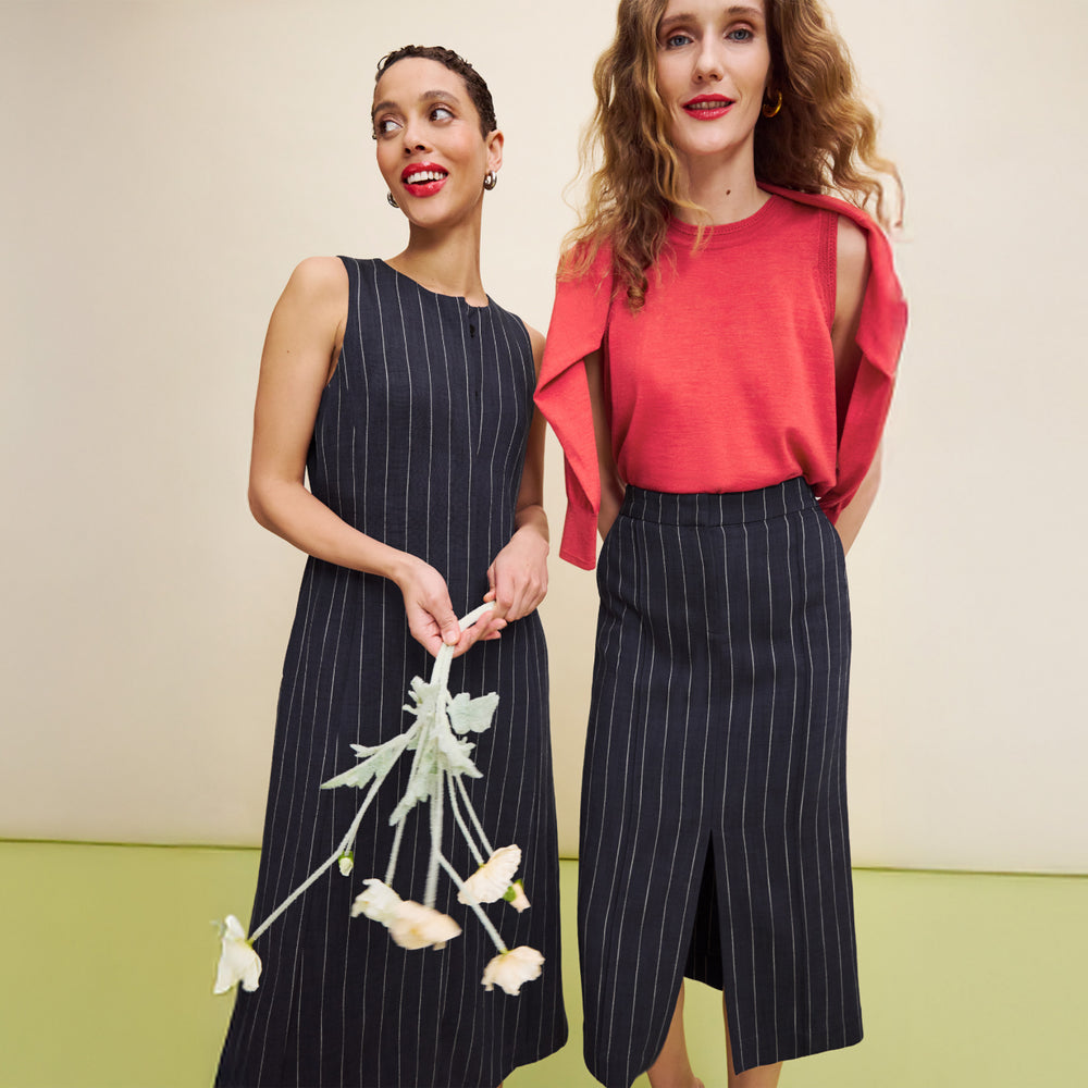 two woman wearing the renata striped dress, meghan skirt striped, and jamie tank in coral. One is holding flowers.
