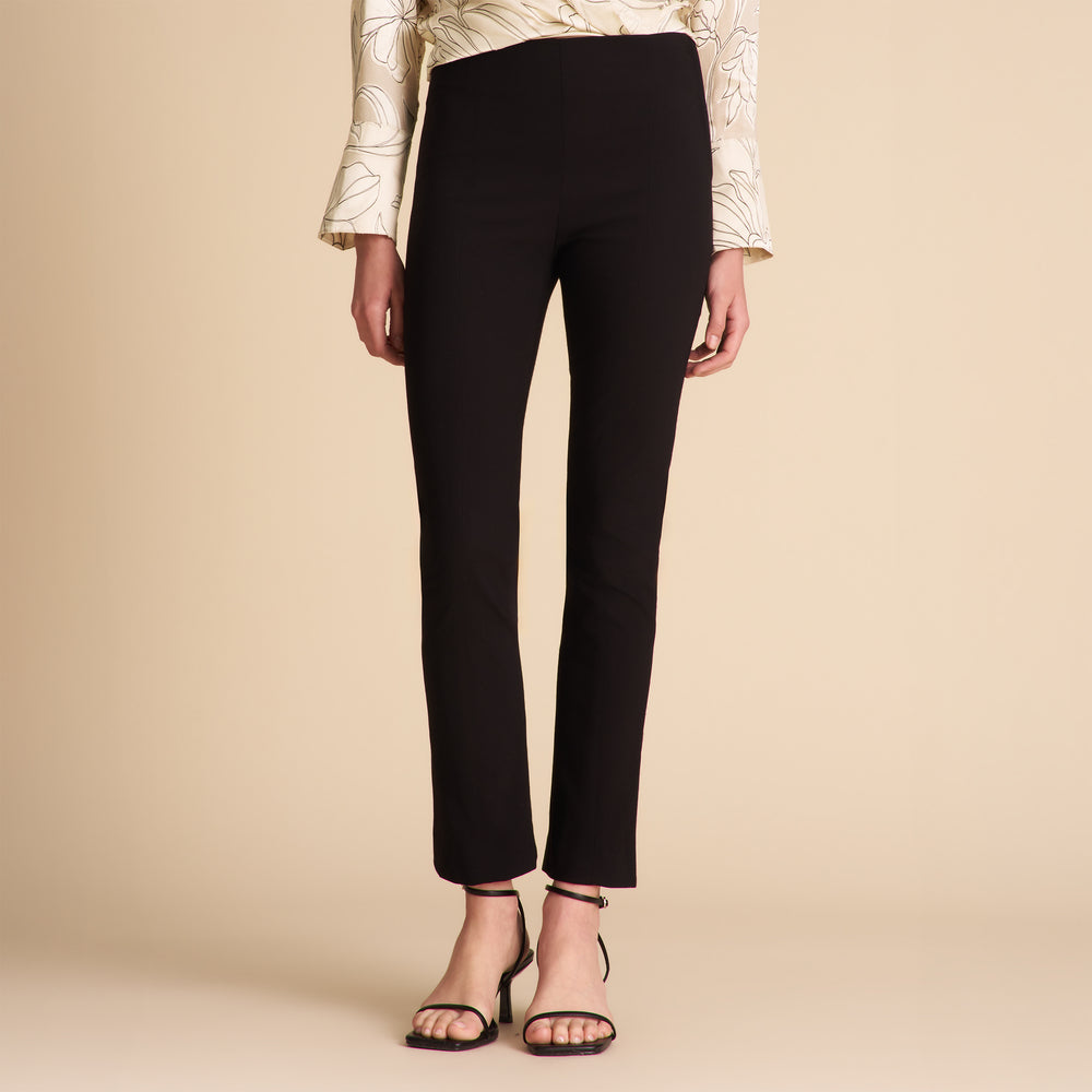 Person wearing black pants and a patterned top on a beige background