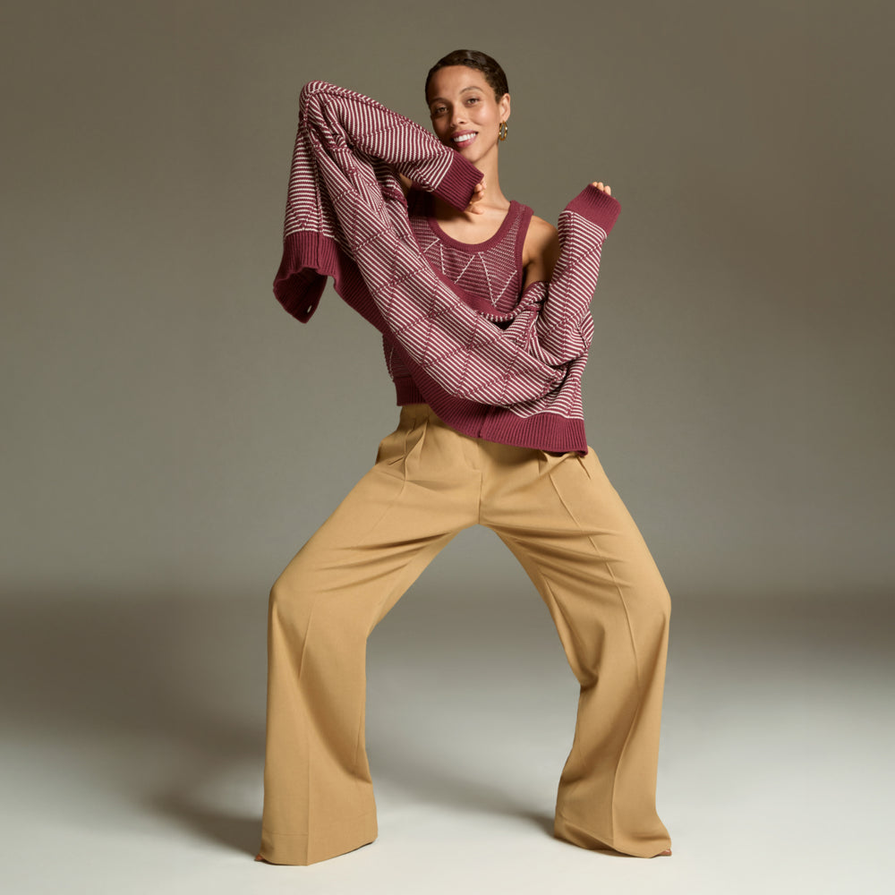 Person wearing a maroon sweater and beige pants against a neutral background