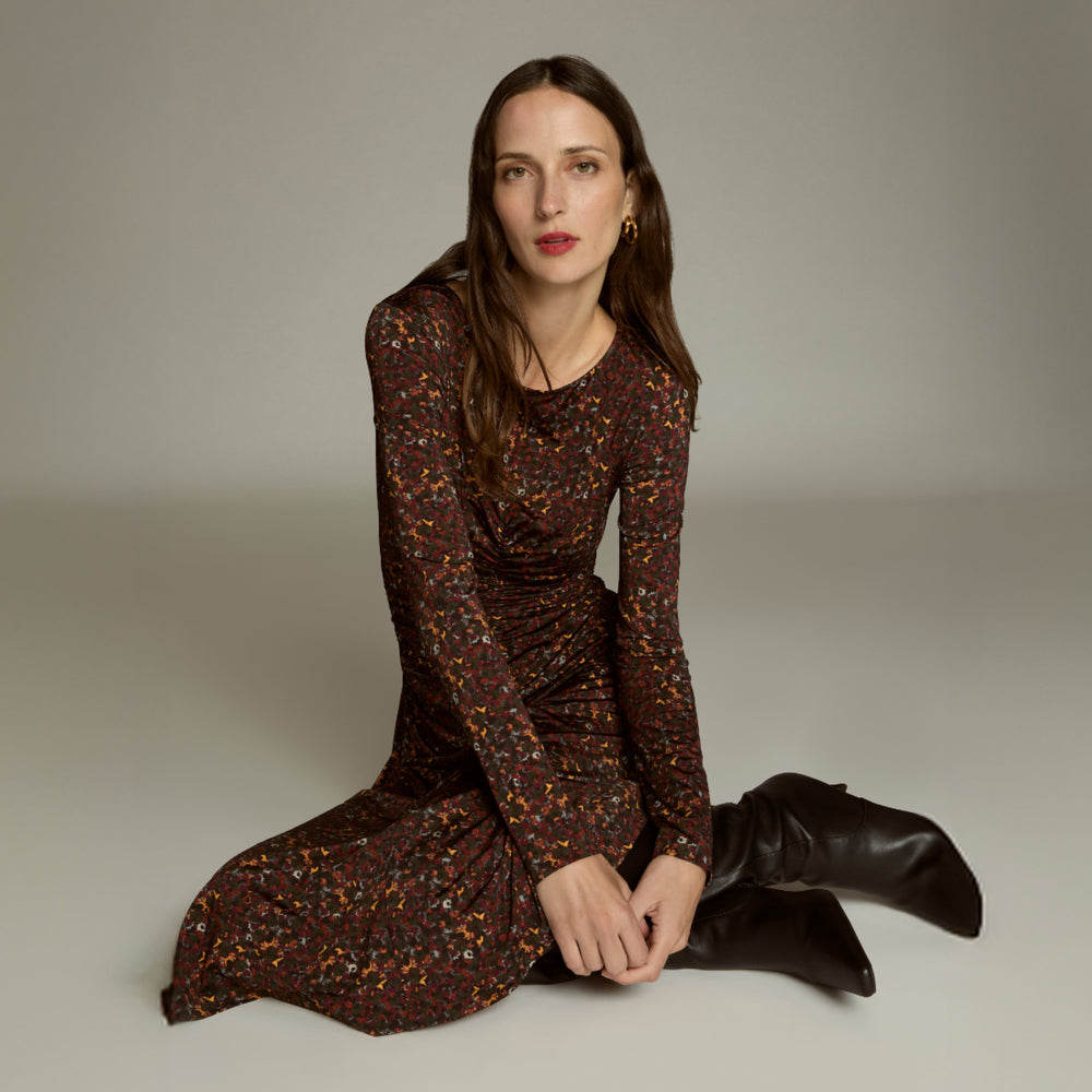 Woman wearing a patterned dress and black boots sitting on a neutral background