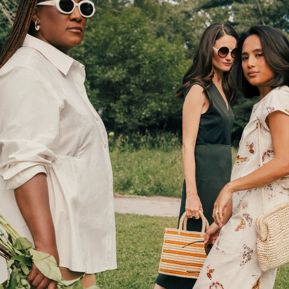 Three women standing outdoors with greenery in the background