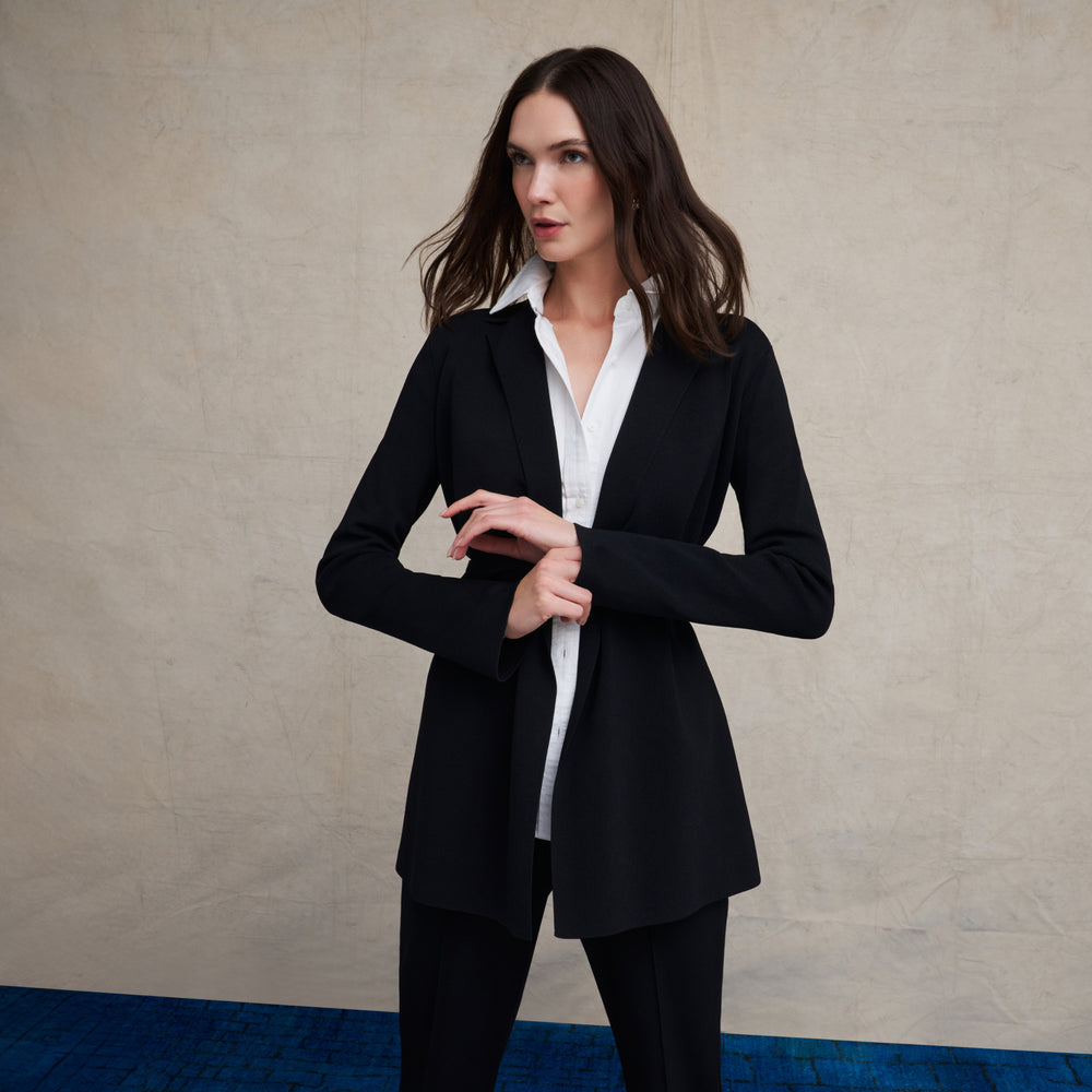 Woman wearing a white long sleeve button down and skinny black pants on a blue carpet floor and against a beige background