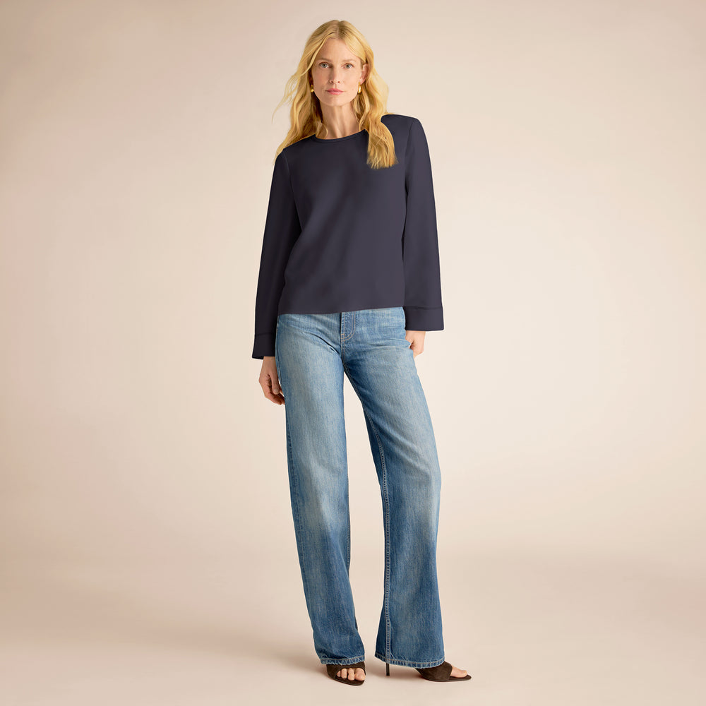 Woman wearing a navy sweater and blue jeans on a beige background