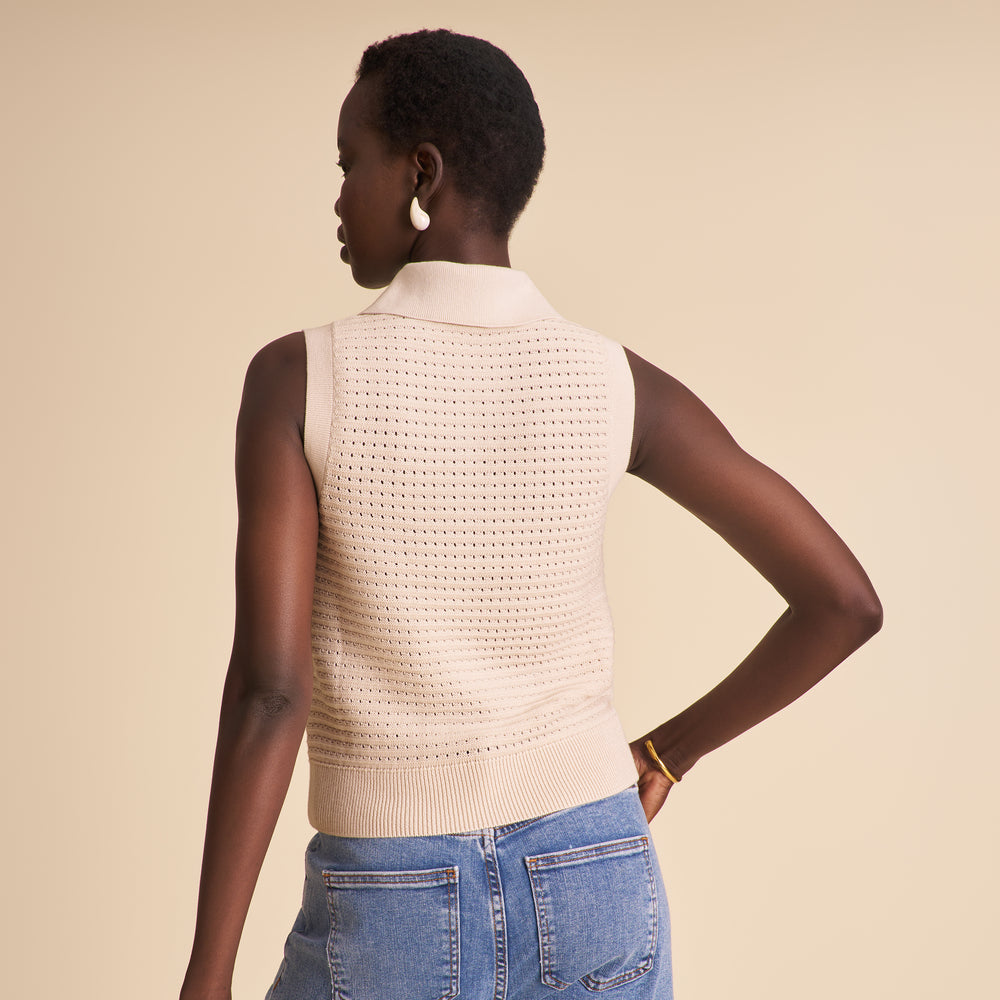 Woman wearing a beige knitted vest and blue jeans on a beige background