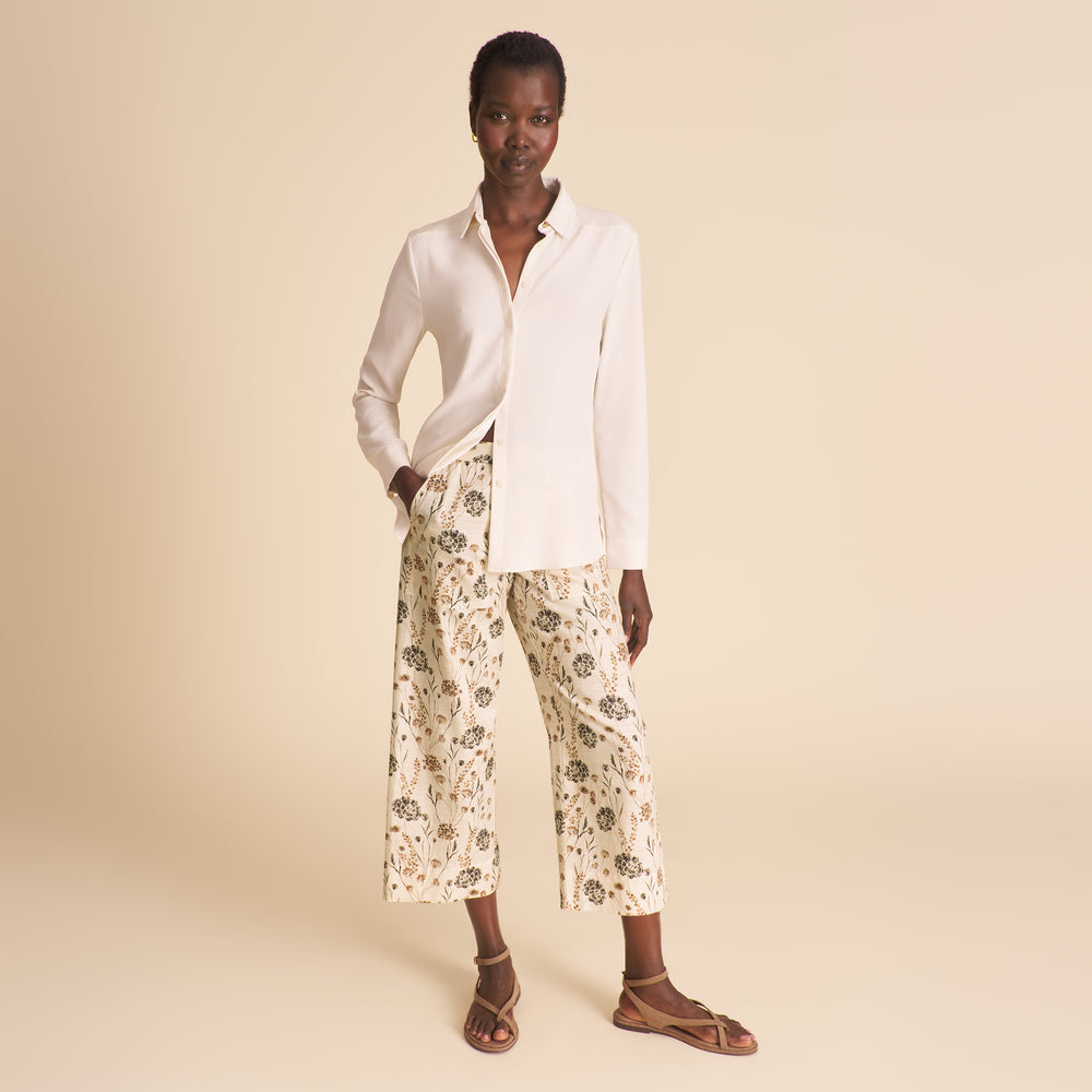 Image of woman wearing a white button down shirt and floral pants on a beige background