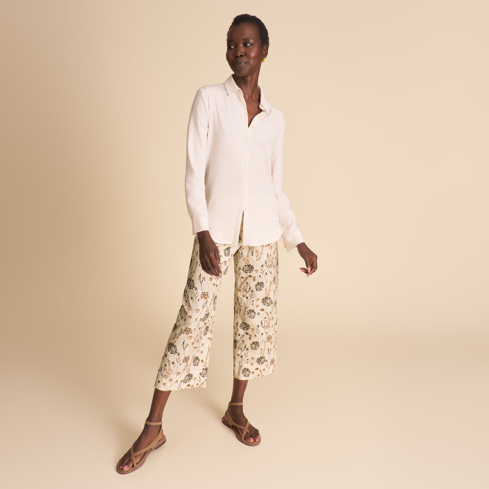 Image of woman wearing a white button down shirt and floral pants on a beige background