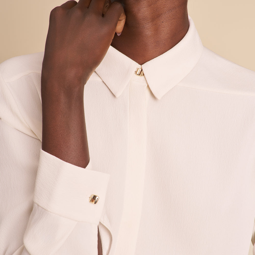 Image of woman wearing a white button down shirt and floral pants on a beige background