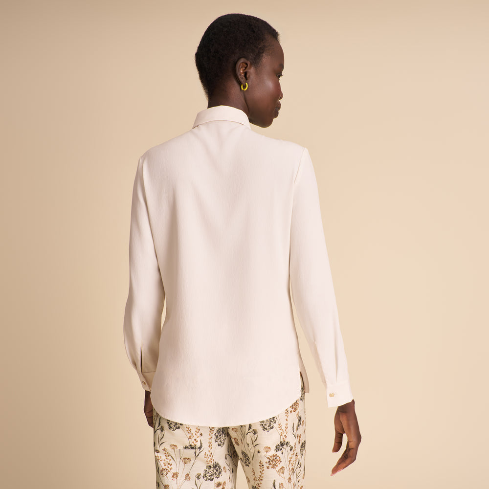 Image of woman wearing a white button down shirt and floral pants on a beige background