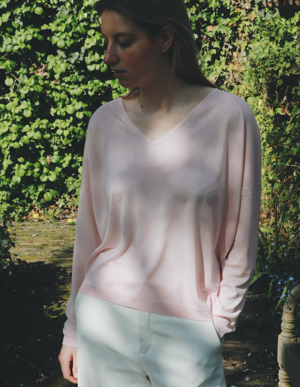 Woman wearing a light pink sweater in a garden setting