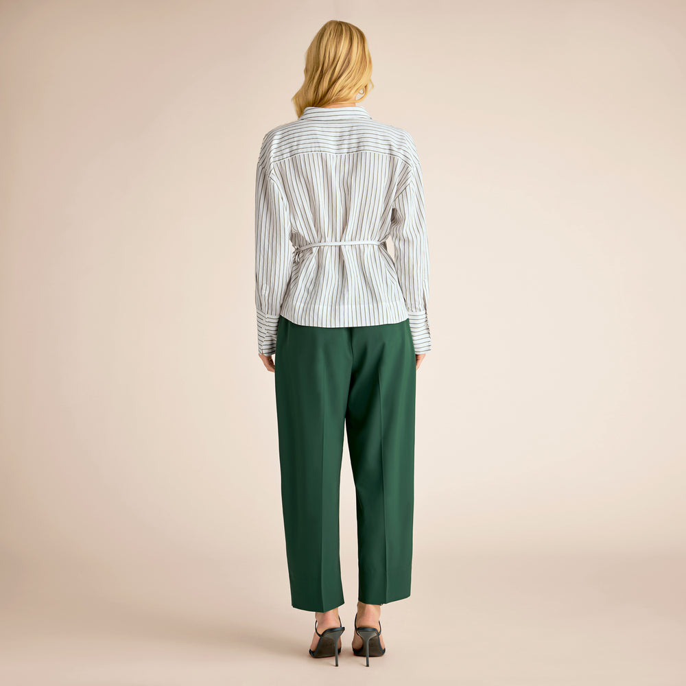 Person wearing a striped shirt and green pants on a beige background