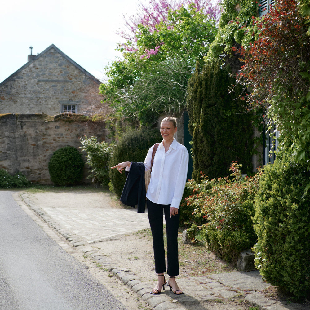 Woman standing on a path with greenery and a building in the background