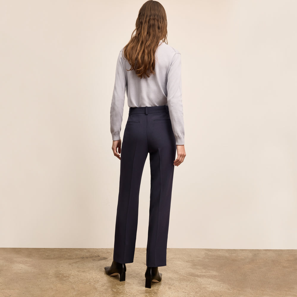 Person wearing a light gray shirt and dark blue pants against a beige wall.