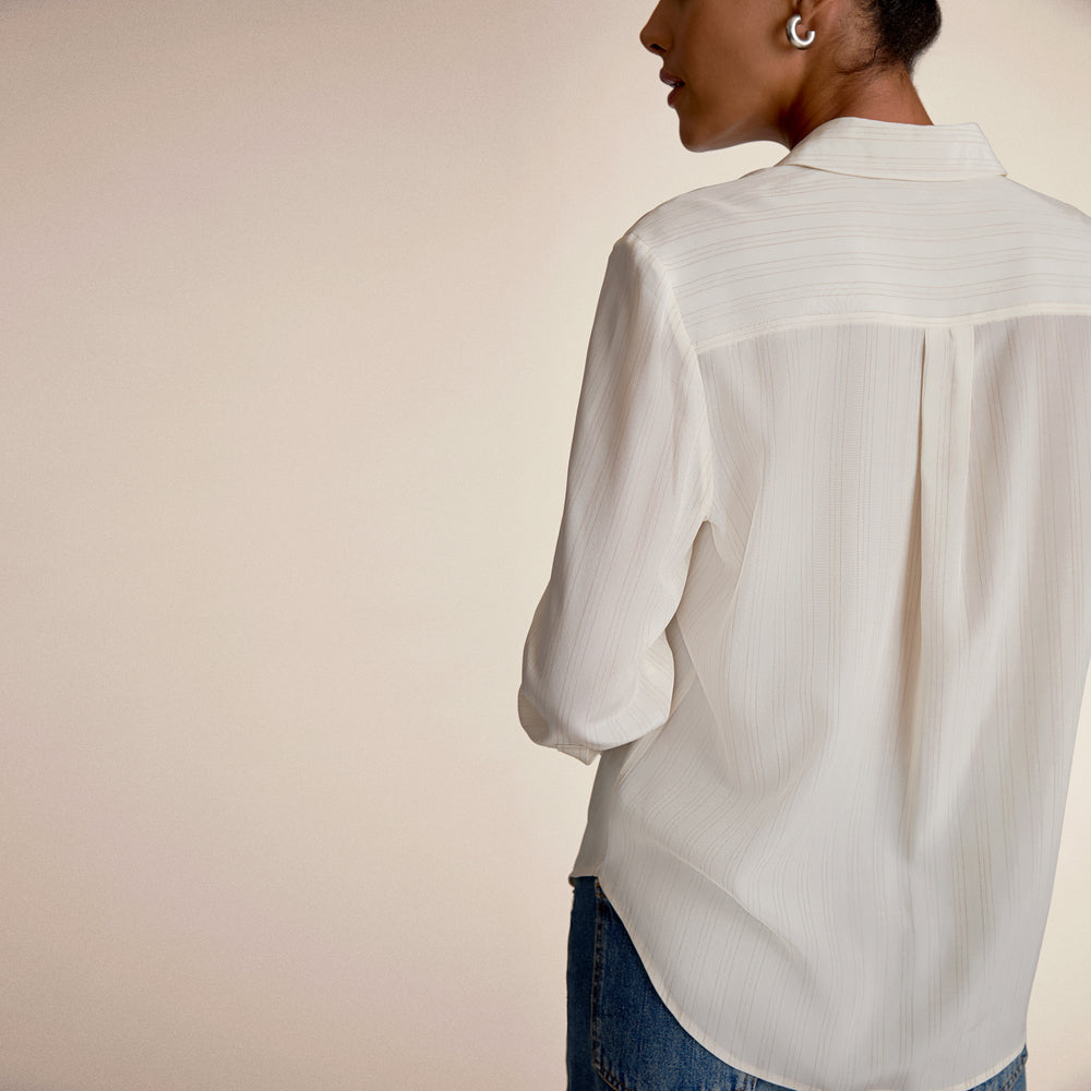 Person wearing a light-colored shirt and jeans against a plain background