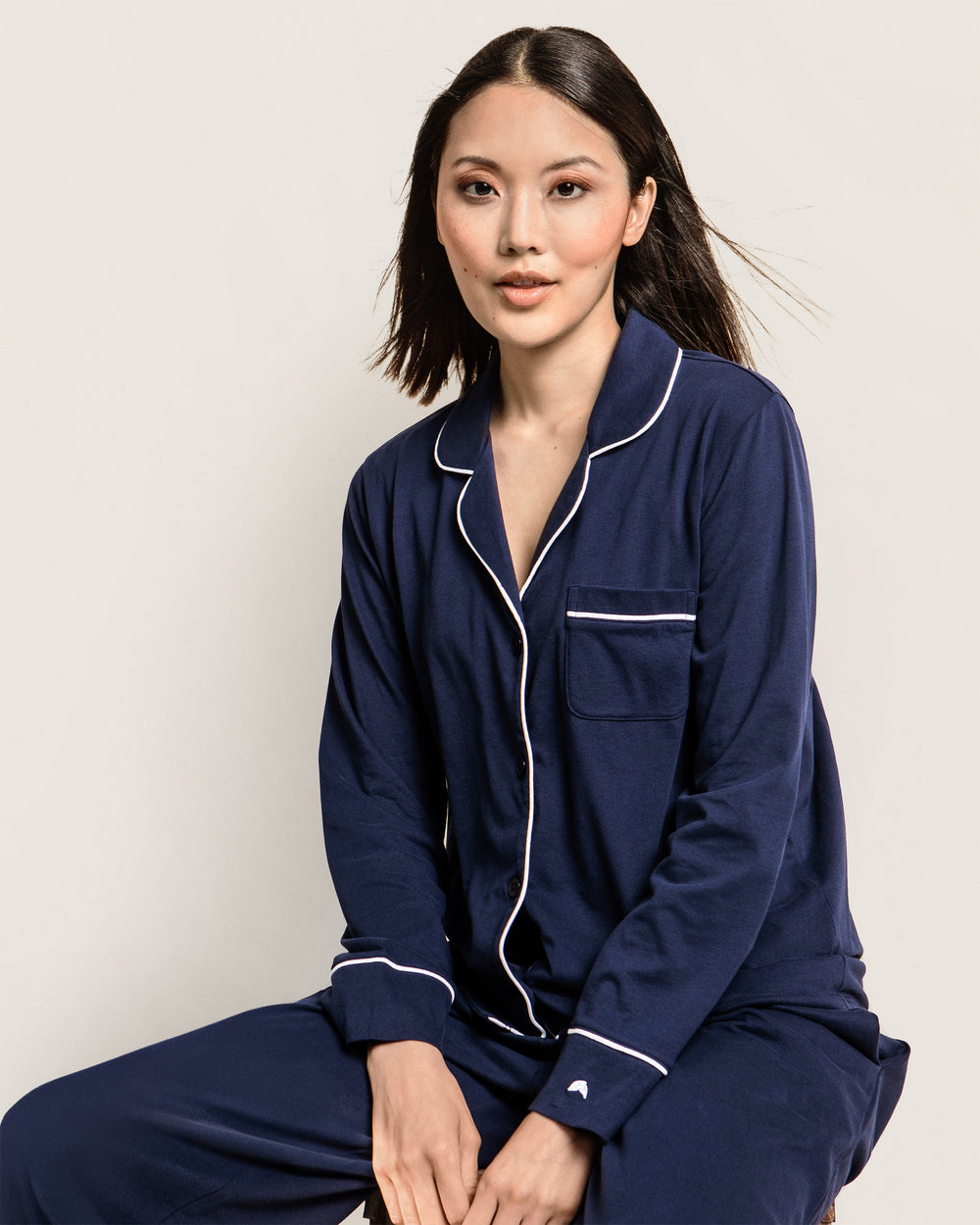 Woman wearing navy blue pajamas with white piping on a plain background
