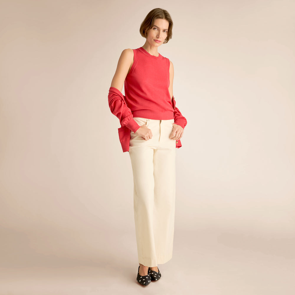 Woman wearing a red sleeveless top and white pants on a beige background