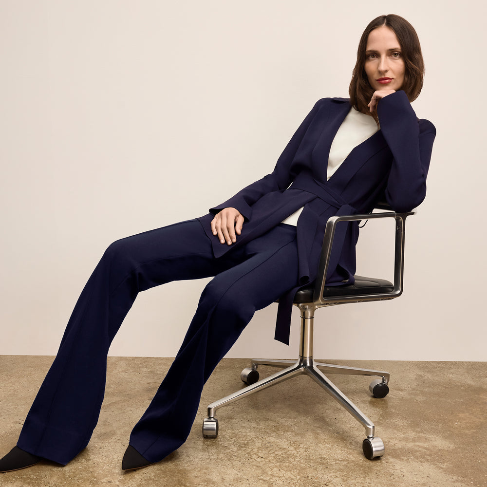 Woman in a navy blue suit sitting on a chair against a plain background