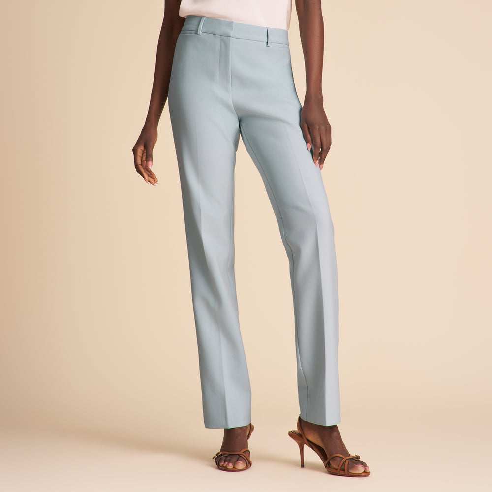 Woman wearing a white top and light blue pants against a beige background