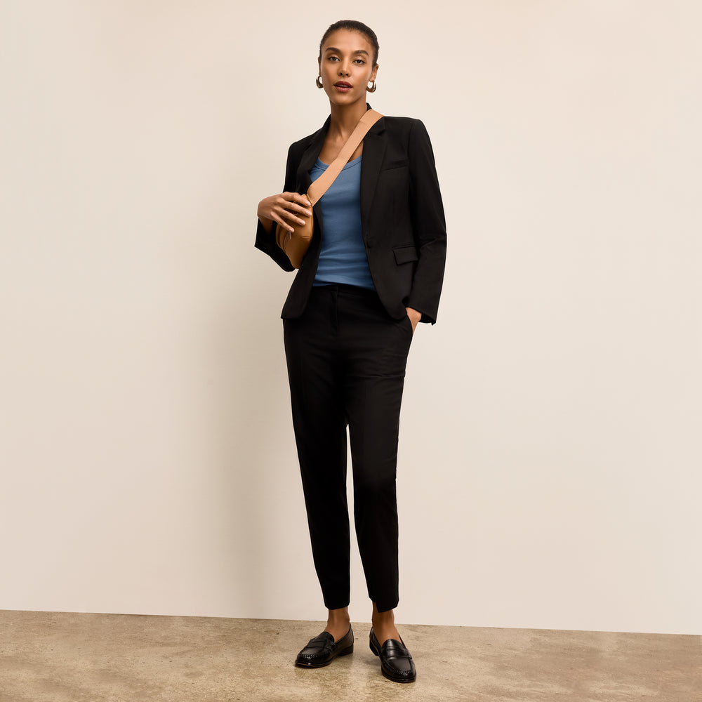 Woman wearing a black suit with a blue top against a beige background