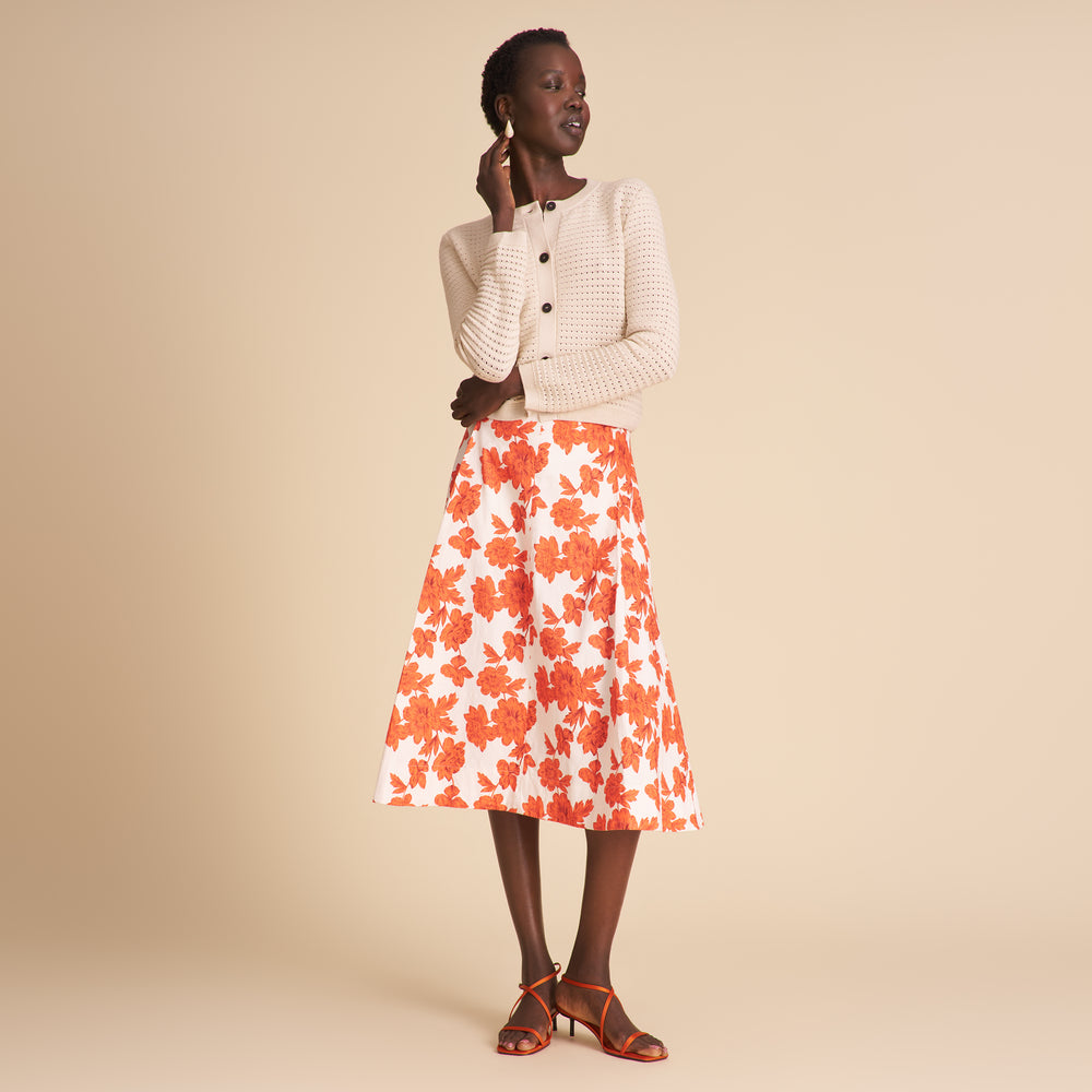 Woman wearing a white cardigan, floral skirt, and high-heeled shoes on a beige background