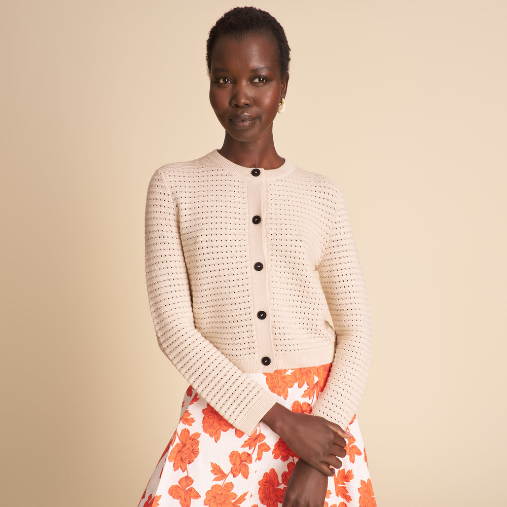Woman wearing a beige knitted cardigan with black buttons and an orange floral skirt on a beige background