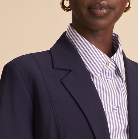 Person wearing a navy blazer over a striped shirt with a beige background