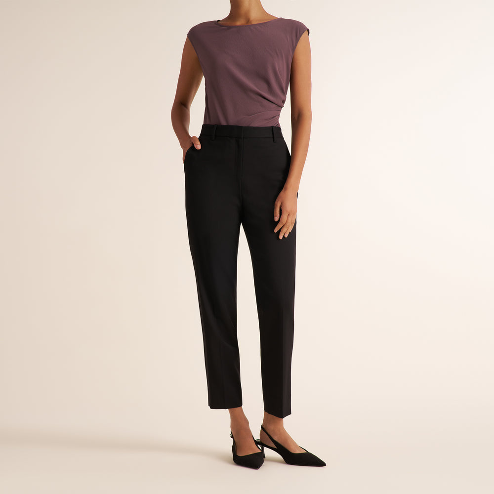 Woman wearing a medium hued purple top with a tailored black blazer and matching tailored pants to make a suit