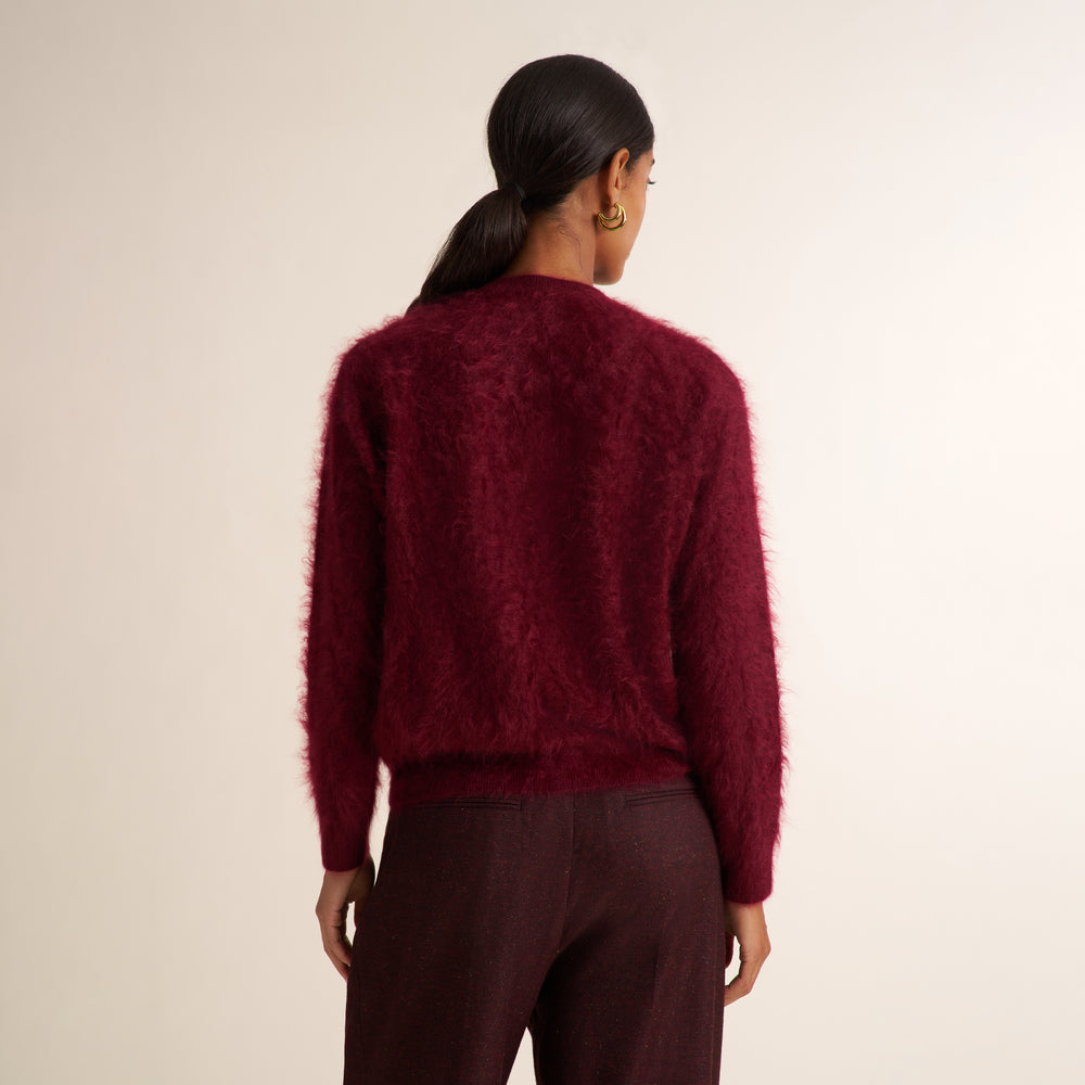 A woman viewed from the back wearing a fuzzy, textured deep burgundy sweater and matching dark trousers against a plain off-white background.