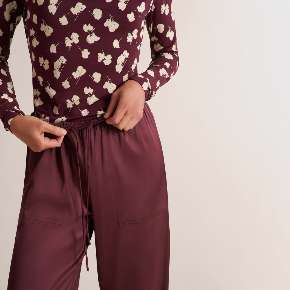 A person wearing a burgundy long-sleeve top with a cream floral print and matching burgundy drawstring pants, shown from the chest down against a plain light background.