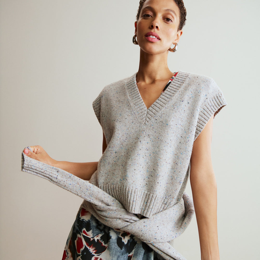Woman wearing a light gray sleeveless sweater over a colorful dress against a neutral background