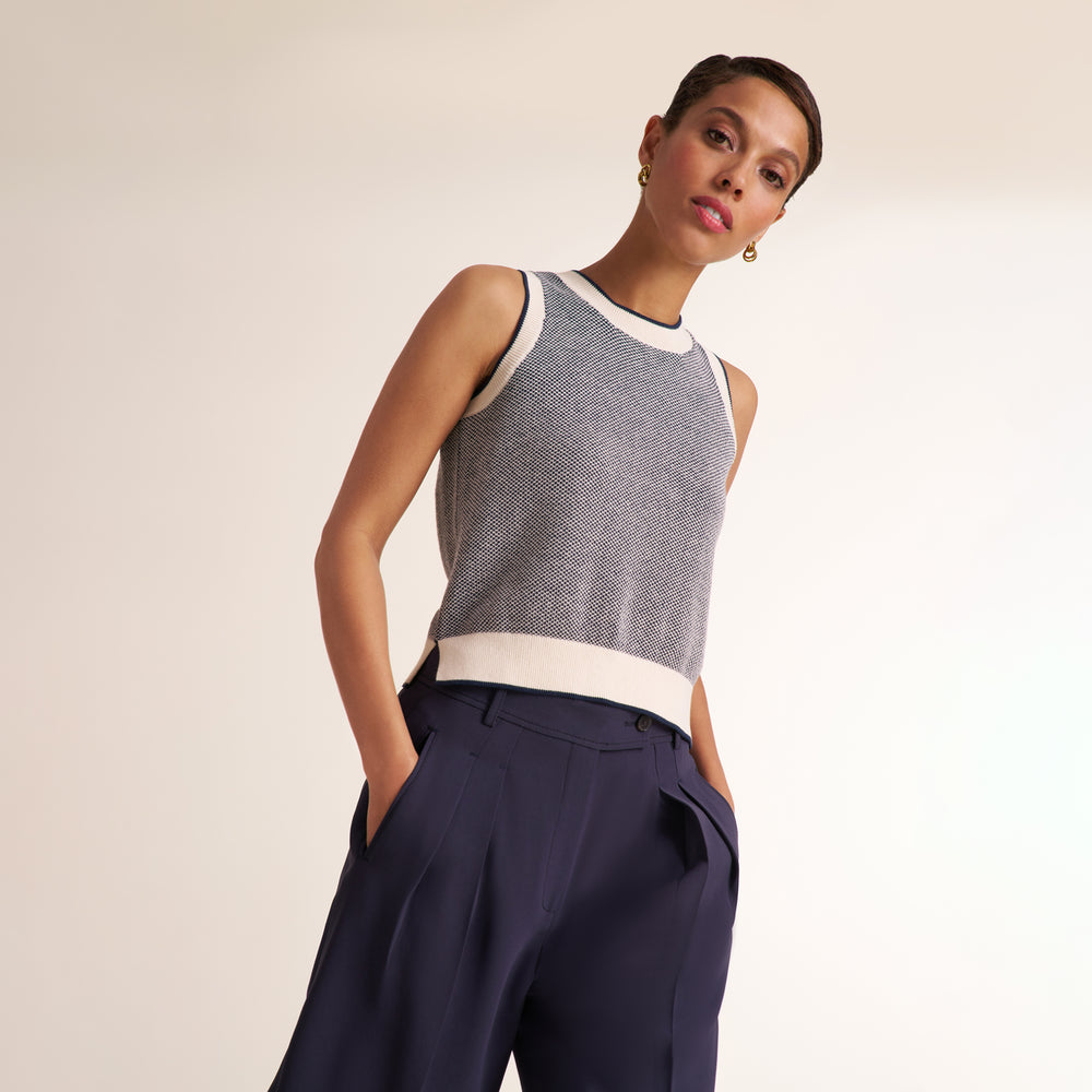 A model wearing a sleeveless textured knit top in gray and white with dark navy wide-leg trousers, photographed against a clean off-white studio background.
