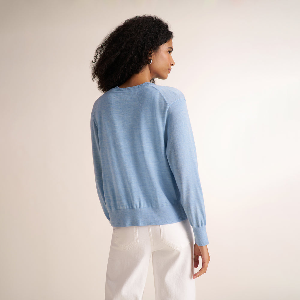 Woman wearing alight blue short sleeve sweater tank with a matching cardigan and wide leg white jeans