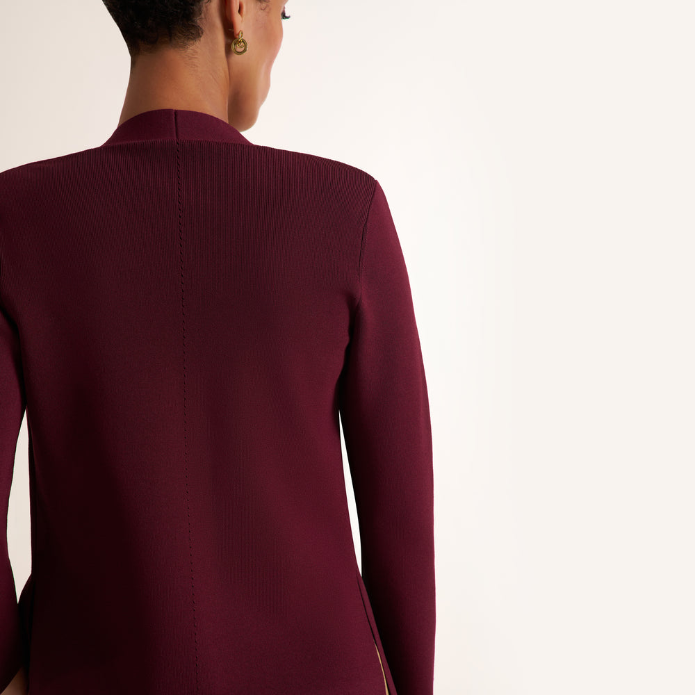 A person shown from the back wearing a long-sleeve burgundy blazer against a plain off-white studio background.
