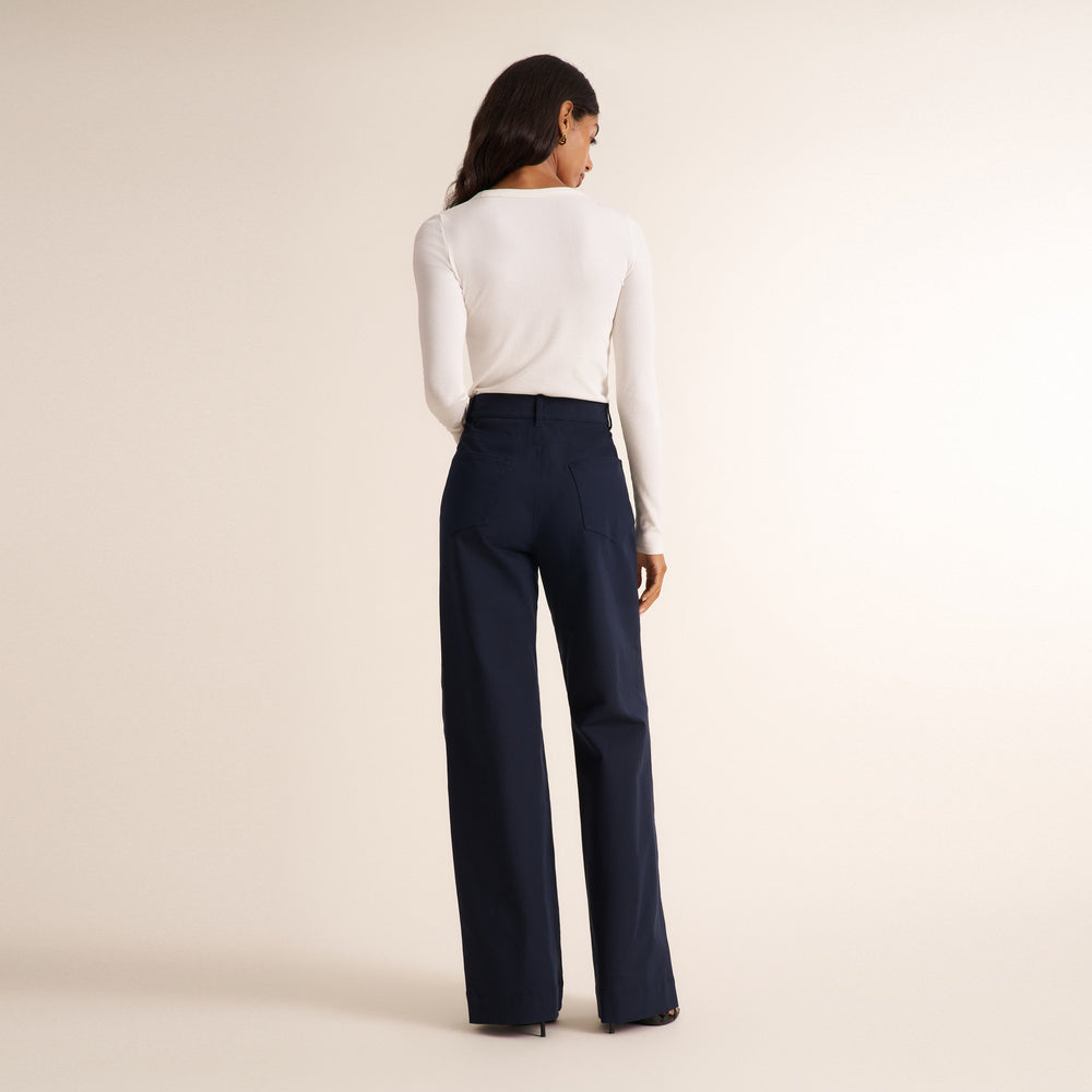 Woman wearing a white long sleeve shirt with dark navy wide leg pants on a neutral background