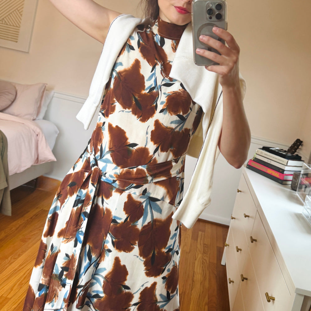Person wearing a floral dress with brown and blue patterns in a bedroom setting.