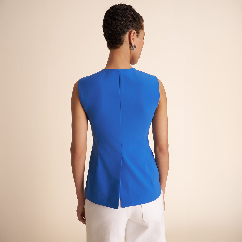 Woman wearing a blue sleeveless top and white pants on a beige background