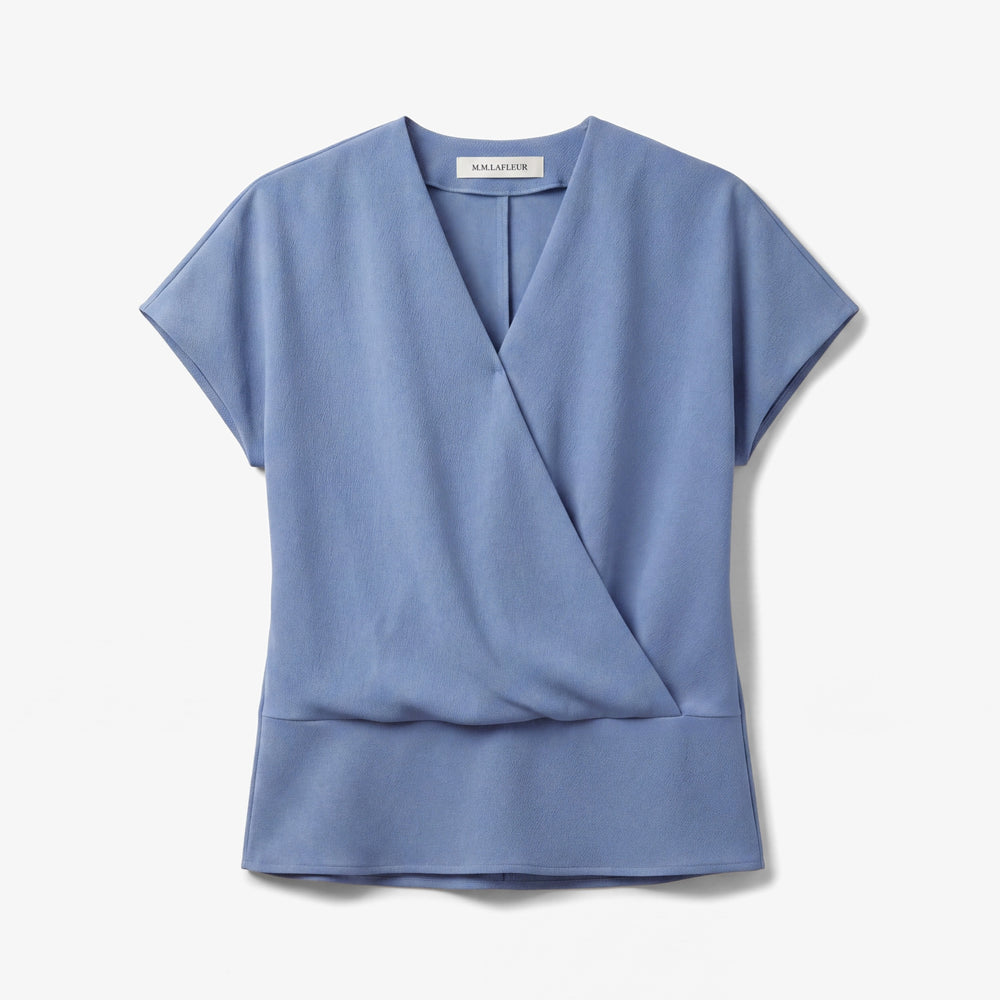 A light blue short-sleeve wrap-style top with a V-neckline and a structured waist seam, shown flat against a light gray background. The brand name 'SALVATORE' is visible on the inner neck label.