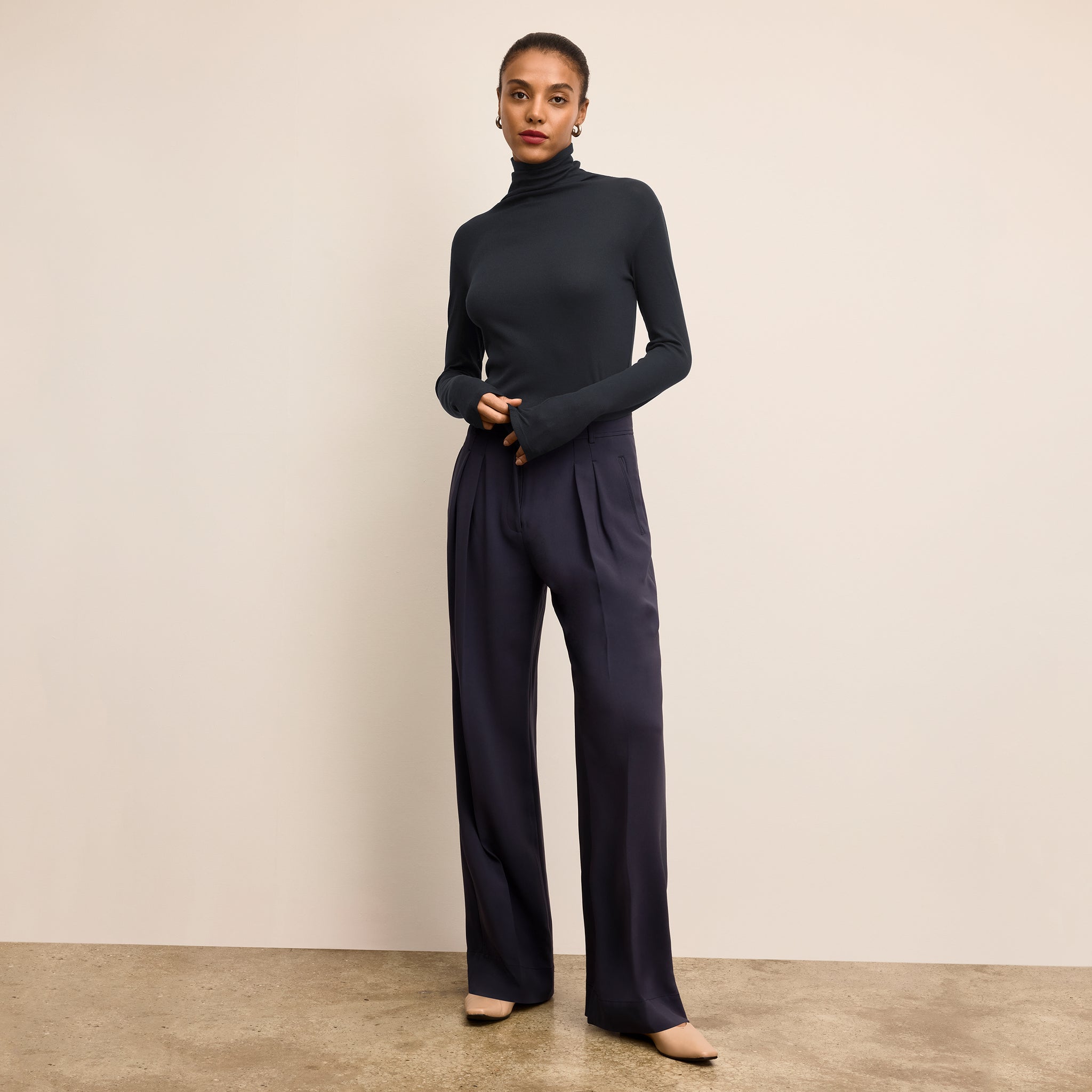 Woman wearing a black turtleneck and pants against a beige background