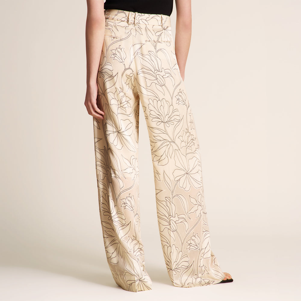 Beige pants with floral pattern worn by a person on a plain background