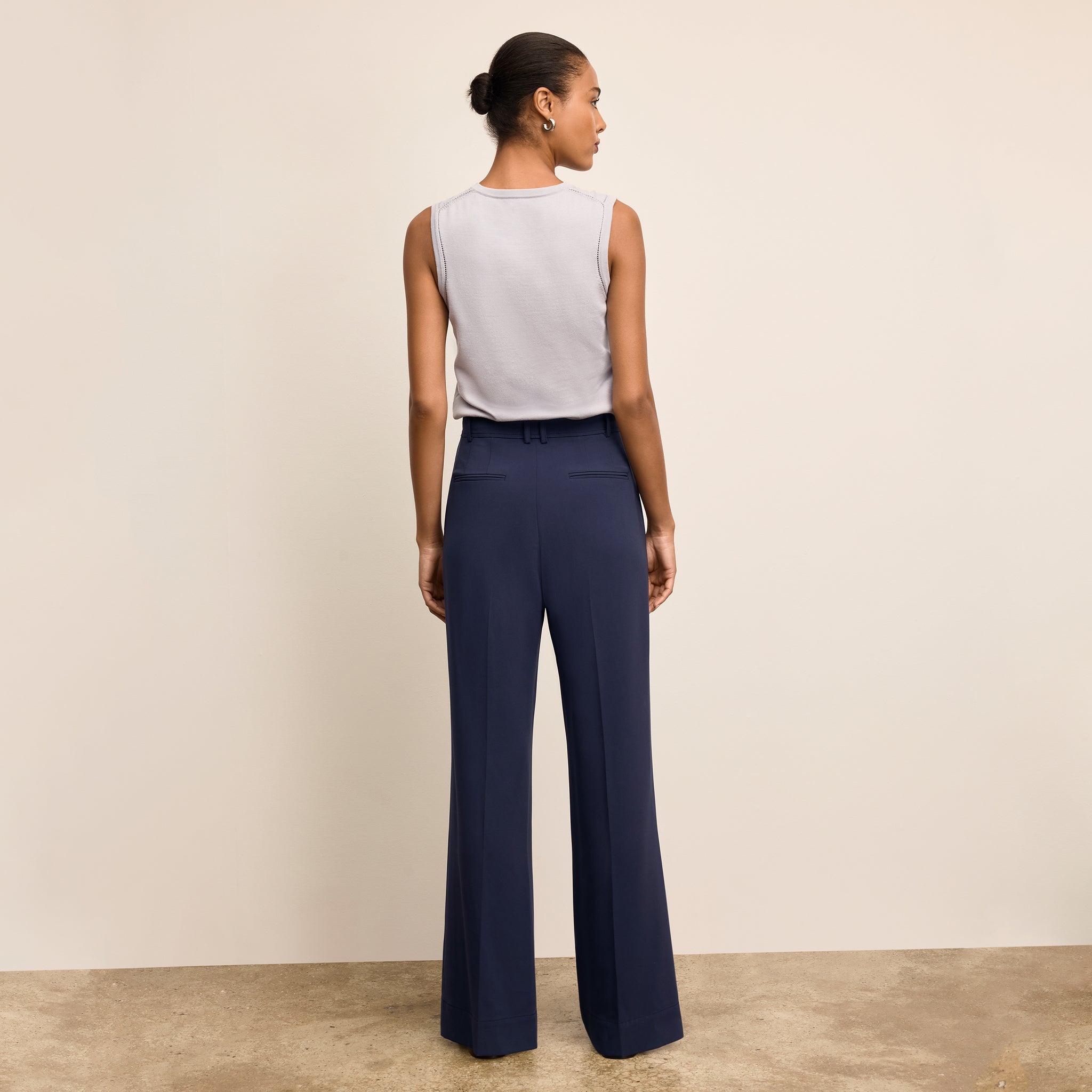 Woman wearing a white sleeveless top and navy pants against a beige background
